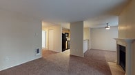 This single-story residence offers a practical and comfortable layout designed for everyday living. The open living and dining area is finished with plush wall-to-wall carpeting and features a classic fireplace with a white mantel, creating a welcoming focal point. A sliding glass door fills the space with natural light and provides direct access to an outdoor patio area. The kitchen is efficiently laid out with light wood cabinetry, light-toned countertops, and a suite of black appliances including an electric range, over-the-range microwave, and refrigerator. A pass-through counter connects the kitchen to the adjacent living space, enhancing the open feel. The bedrooms are generously sized, each carpeted and painted in warm neutral tones. Several bedrooms include built-in closets with sliding or bifold doors, and windows that invite natural light. Baseboard heaters are present throughout the bedrooms for efficient climate control. The bathroom is neatly appointed with a light wood vanity, a large mirror, and a full tub-shower combination with chrome fixtures. Durable wood-look flooring in the bathroom adds a clean, contemporary contrast to the carpeted areas throughout the rest of the home.