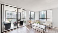 This well-appointed 2-bedroom, 1-bathroom urban residence offers a thoughtfully designed layout bathed in natural light. The living room is a standout space, featuring expansive floor-to-ceiling windows framed in dark bronze and a glass-enclosed balcony accessed through sliding doors. The balcony extends the living area outdoors, furnished for relaxation while offering panoramic views of the surrounding cityscape. Light hardwood flooring flows throughout, complementing the bright, neutral palette of the interiors.

The kitchen is efficiently designed with stainless steel appliances, white subway tile backsplash, and ample cabinetry. A convenient in-unit stacked washer and dryer is tucked adjacent to the kitchen. The primary bedroom is a comfortable retreat, featuring large corner windows that wrap around to frame unobstructed city views and fill the room with natural light. The second bedroom also benefits from a large window with urban views and includes a built-in closet. The bathroom is finished with granite countertops, grey cabinetry, a full-size soaker tub with shower, and large mirror. The overall ambiance is modern, clean, and urban, making this a practical and stylish city residence.