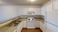 This single-floor residence in North Charleston, South Carolina offers a straightforward and functional layout designed for comfortable everyday living. The kitchen features a U-shaped configuration with white cabinetry extending to the ceiling, providing generous storage throughout. Neutral-toned laminate countertops complement the white appliances, which include an electric coil range, over-the-range microwave, and refrigerator. A double-basin stainless steel sink sits beneath the cabinetry, and wood-look flooring grounds the space with a warm, practical finish.

The living area is open and inviting, finished with plush wall-to-wall carpeting and a textured ceiling. Large windows and a glass-paneled door allow natural light to fill the room, creating a bright and airy atmosphere. The bedroom mirrors this aesthetic, with soft carpeting, a centered ceiling light fixture, and a window that brings in additional daylight.

The bathroom is efficiently designed, featuring a single-sink vanity with white cabinetry and a large mirror, a tall linen storage cabinet, wood-look flooring, and a separate bathtub and shower area. The overall layout of the unit, as seen in the dollhouse view, is compact yet well-organized, with a clear distinction between living, sleeping, kitchen, and bathroom spaces.