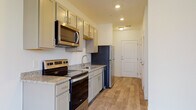 Located at 210 W Fifth Ave in Columbus, Ohio's vibrant Short North neighborhood, this single-floor unit offers a thoughtfully designed open layout with modern finishes throughout. Light-toned luxury vinyl plank flooring runs consistently across the living and kitchen areas, creating a cohesive and easy-to-maintain interior.

The kitchen is well-appointed with gray cabinetry, granite-style countertops, and a full suite of stainless steel appliances including an electric range, over-the-range microwave, dishwasher, and refrigerator. A stainless steel sink with a modern faucet completes the functional workspace. The kitchen flows seamlessly into the open living area, which is filled with natural light from large windows and a set of French doors that provide direct access to an outdoor space.

The bathroom area features wood-look vinyl flooring and leads to a walk-in closet with a built-in shelving and hanging rod system, offering generous storage. Additional storage is accessible via a louvered-door closet near the entryway. Recessed lighting throughout the unit ensures bright, even illumination. The neutral white and beige color palette, combined with clean architectural lines, gives the space a fresh, contemporary ambiance well-suited for modern living.