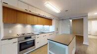 This single-floor residence showcases a thoughtfully designed contemporary interior with clean lines and a neutral palette throughout. The kitchen is a standout feature, outfitted with flat-front cabinetry in a combination of crisp white and warm wood tones, complemented by under-cabinet LED lighting and a classic subway tile backsplash. Stainless steel Bosch appliances, including a gas range, wall oven, and built-in microwave, are seamlessly integrated into the layout. A central island with a dark countertop provides additional prep and storage space, while a glass sliding barn door adds a modern architectural touch connecting the kitchen to adjacent areas.

The living areas are finished with light-toned hardwood flooring that extends throughout, creating a cohesive and airy feel. Floor-to-ceiling windows and a glass balcony door flood the space with natural light and frame urban skyline views. The bedroom also benefits from large windows offering sweeping city vistas.

Two bathrooms mirror the modern aesthetic, each featuring large-format porcelain tile flooring, floating wood vanities with white countertops, and clean white walls. One bathroom includes a tiled walk-in shower. The overall ambiance is bright, minimal, and polished.