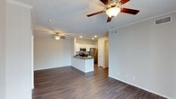 This single-floor residence offers a thoughtfully designed open-concept layout that seamlessly connects the living area and kitchen, creating a spacious and airy atmosphere. The rich, dark hardwood-style flooring extends throughout the main living space, adding warmth and a modern aesthetic.

The kitchen is a standout feature, outfitted with stainless steel appliances including a refrigerator, microwave, and range. White cabinetry provides ample storage, while a peninsula island with a dark countertop serves as both a functional workspace and a natural dividing point between the kitchen and living area. Recessed lighting illuminates the kitchen, complementing the overall bright and clean design.

The living area is generously proportioned, offering flexible furniture arrangements. Ceiling fans are installed throughout, enhancing airflow and comfort. Crown molding adds a refined architectural detail along the ceiling line, while neutral-toned walls create a versatile backdrop for any interior style. The layout also features a hallway leading to additional rooms, hinting at a well-organized and functional floor plan. Overall, the space strikes a balance between modern finishes and practical design.