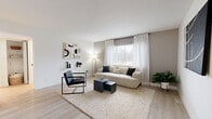 This single-floor residence offers three bedrooms, one bathroom, a living room, kitchen, and hallway, all unified by a clean, modern aesthetic. Light wood-tone flooring runs throughout, complementing the crisp white walls and creating a bright, airy atmosphere.

The living room is a welcoming space featuring a large window dressed with sheer white curtains that invite natural light, while the neutral tones and minimalist decor lend a calm, contemporary feel. The space flows openly toward the entry and kitchen area.

The kitchen is well-equipped with two-tone cabinetry — white upper cabinets with gold hardware and dark lower cabinets — paired with a striking marble-style backsplash and stainless steel appliances, including a gas range, dishwasher, and refrigerator. A shiplap-style accent wall adds texture and character.

The primary bedroom is a comfortable, well-lit retreat with two windows offering neighborhood views and recessed lighting overhead. The two additional bedrooms maintain the same clean, bright design, each featuring recessed lighting, light flooring, and windows with natural light.

The bathroom is finished with a dark vanity accented by gold hardware, a white countertop, and a full tub-shower combination with a subway tile surround and matte black fixtures, offering a stylish and functional space.