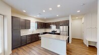 Located at 201 Wildwood Blvd in Forney, TX, this thoughtfully designed single-story residence offers a comfortable and modern living experience. The open-concept kitchen and living area serves as the heart of the home, showcasing rich dark espresso cabinetry, granite countertops, and a full suite of stainless steel appliances including a refrigerator, electric range, and dishwasher. A central kitchen island provides additional prep space and casual seating, while recessed lighting and wood-style flooring throughout lend a clean, contemporary aesthetic. The bedroom is a serene retreat finished with plush carpet and a ceiling fan, offering a cozy and restful atmosphere. It connects to a spacious walk-in closet outfitted with multiple hanging rods and built-in shelving for generous storage. The full bathroom features dark cabinetry consistent with the kitchen's design, a wide vanity with a white countertop, a large mirror, and a tiled shower. A dedicated laundry area with hookups adds everyday convenience, and the bright, neutral color palette throughout creates an inviting and cohesive feel across the entire home.