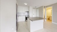Located on Rue Sherbrooke Est in the heart of Montréal, this modern studio offers a thoughtfully designed open-concept layout that efficiently combines the living and kitchen areas into a cohesive, airy space. Light-toned hardwood-style flooring runs throughout, complementing the clean white walls and creating a bright, minimalist aesthetic.

The kitchen is well-appointed with sleek white cabinetry extending to the ceiling for ample storage, a white subway tile backsplash, stainless steel appliances including a refrigerator, dishwasher, and range, and a central island with a grey concrete-style countertop that doubles as a breakfast bar. The open living area benefits from large floor-to-ceiling windows that flood the space with natural light and frame expansive views of the Montréal skyline and surrounding cityscape.

A separate sleeping area features mirrored sliding closet doors that enhance the sense of space, along with neutral warm-toned walls and continued light flooring. The bathroom is finished with full white ceramic tile surrounding a soaking bathtub and shower combination, maintaining the clean and contemporary feel found throughout the unit.

Overall, this studio presents a cohesive, modern design with a neutral palette, abundant natural light, and functional use of space in a prime Montréal location.