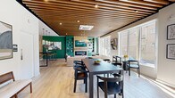 Located at 821 East Main Street in Stamford, Connecticut, The Lafayette's amenity lounge is a thoughtfully designed single-floor communal space that blends modern aesthetics with functional versatility. The interior is anchored by striking slatted wood ceiling panels that run throughout, adding warmth and architectural character to the open-plan layout. Light hardwood flooring complements the natural tones of the ceiling and connects the various zones seamlessly.

The central lounge area features a stone-surround fireplace flanked by bold emerald green built-in shelving, creating a vibrant focal point. A large flat-screen display is mounted above the fireplace, and comfortable seating is arranged to foster conversation and relaxation. Oversized windows along the perimeter flood the space with abundant natural light and offer views of the surrounding streetscape.

A stylish wet bar area is equipped with a beverage cooler, dark countertops, a decorative tile backsplash, and wood-paneled accent walls, illuminated by elegant glass pendant lights. A high-top bar table with leather-and-metal stools provides casual seating nearby.

A dedicated dining area with a dark wood table and matching chairs offers a more structured gathering space. Toward the rear, a bright and open children's play area provides a welcoming environment for younger residents. Curated artwork displayed throughout adds a gallery-like quality to the overall ambiance.