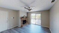 This single-floor residence offers a well-organized layout with a cohesive design carried throughout each room. The living area serves as the focal point of the space, anchored by a classic brick fireplace with a wood mantle and raised hearth. A ceiling fan with a brushed nickel finish is centrally positioned overhead, complementing the textured ceiling. A full-height sliding glass door fitted with vertical blinds opens to a balcony, allowing natural light to fill the room and offering a view of surrounding greenery. Wood-look laminate flooring runs continuously through the living area, bedrooms, and connecting spaces, lending a clean and unified aesthetic.

The kitchen follows a galley-style configuration, featuring crisp white shaker cabinetry on both sides, granite-patterned countertops, and stainless steel appliances including a dishwasher, range, and refrigerator. A closet at the end of the kitchen provides additional storage. The bedroom is a quiet, well-proportioned room with a window fitted with horizontal blinds and the same wood-look flooring. The bathroom includes a granite-topped vanity with an undermount sink, white cabinetry, a large mirror, and a Hollywood-style light bar. Throughout, neutral wall tones and clean finishes create a calm, functional atmosphere.