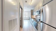 This single-floor studio is designed with a clean, contemporary aesthetic that maximizes every inch of its compact footprint. Light wood-style flooring runs seamlessly throughout, complementing the crisp white walls and creating a bright, cohesive atmosphere.

The galley-style kitchen is a standout feature, outfitted with a full suite of stainless steel appliances — including a refrigerator, range, microwave, and dishwasher — paired with gray shaker-style cabinetry, granite countertops, and a tile backsplash. Track lighting illuminates the workspace, while an adjacent peninsula with additional cabinetry and counter space offers extra functionality.

The open living area benefits from a large window that invites natural light and provides views of the surrounding neighborhood. The space is versatile and well-suited for both relaxing and working from home.

The bathroom continues the modern design language, featuring gray cabinetry with granite countertops, a wall-mounted mirror, and wood-style flooring. A grab bar adds accessibility-conscious detail.

A hallway connects the rooms, lined with closet doors for built-in storage. An electrical panel is conveniently recessed into the wall. Overall, the studio presents a polished, move-in-ready living environment with quality finishes throughout.
