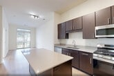 Located at 100 Rosie Square in Wood-Ridge, NJ, this one-bedroom, one-bathroom residence offers a thoughtfully designed single-floor layout with a clean, modern aesthetic throughout. The open-concept kitchen and living area serves as the heart of the home, featuring rich dark-brown cabinetry, a white subway tile backsplash, light quartz countertops, and a full suite of stainless steel appliances including a gas range, built-in microwave, dishwasher, and refrigerator. A central kitchen island provides additional workspace and storage. Light hardwood flooring extends throughout the entire residence, lending warmth and visual continuity. The living area is bright and airy, benefiting from a large sliding glass door that frames outdoor greenery and fills the space with natural light. The bedroom is a comfortable size, equipped with a large window overlooking the exterior and access to a walk-in closet with built-in wire shelving for organized storage. A second closet provides additional space. The bathroom features a white vanity with under-cabinet storage, a well-lit mirror, and a clean, neutral finish. Additional conveniences include an in-unit laundry area and a utility room, making this a fully functional and efficiently organized residence.