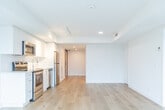 Located on College Street in Toronto's dynamic Harbord Village neighbourhood, this modern one-bedroom, one-bathroom unit offers a thoughtfully designed single-level layout. The interior is defined by a clean, minimalist aesthetic, featuring wide-plank light hardwood flooring and crisp white walls throughout that create a bright, open atmosphere.

The living area is a standout feature, anchored by expansive floor-to-ceiling windows with bold black frames that flood the space with natural light and offer unobstructed views of the vibrant College Street streetscape below. The open-plan layout connects the living area to the kitchen, which is equipped with stainless steel appliances, including a full-size refrigerator, and features built-in cabinetry and recessed lighting.

The bedroom is a well-proportioned private retreat, accessed via a sleek sliding panel door and featuring its own access to a balcony through a black-framed glass door. The full bathroom is finished in a clean, contemporary style with large-format floor tiles, a white floating vanity with brushed hardware, a full soaker tub with overhead shower, and white subway tile surround. A second living or flex room provides additional versatile space. Recessed lighting and modern ventilation are present throughout.