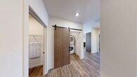 This thoughtfully designed 2-bedroom, 2-bathroom residence is laid out on a single floor, offering a comfortable and efficient living experience. The open-concept kitchen and living area serves as the heart of the home, featuring wood-tone cabinetry with matte black hardware, clean white countertops, and wood-look vinyl flooring that flows throughout the main areas. A sliding glass door opens to a private balcony, filling the living space with natural light and providing views of the surrounding community. The primary bedroom offers generous proportions with large windows fitted with blinds, while the second bedroom features plush wall-to-wall carpeting and its own window for natural light. Both bedrooms are served by well-appointed bathrooms — one featuring a walk-in shower with sliding glass doors and a wood-toned vanity, the other with a full soaking tub and shower combination. A dedicated laundry area with a stacked washer and dryer unit is tucked behind a stylish sliding barn door, adding a contemporary design touch. Adjacent to the laundry, a walk-in closet provides ample wire-shelf storage. Neutral wall tones, consistent flooring materials, and recessed lighting throughout create a cohesive, modern ambiance across the entire residence.