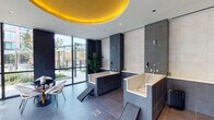 Located in Chicago's West Loop at 22 N Sangamon Street, this single-floor pet amenity space combines contemporary design with highly functional features tailored specifically for pets and their owners. The space is defined by its striking architectural elements, most notably a bold circular yellow ceiling installation that serves as a visual focal point, contrasting dramatically against the otherwise sleek, neutral palette of dark slate-gray tile flooring and large-format light stone wall cladding.

The bathing area is a standout feature, housing multiple walk-in pet bathing tubs constructed with integrated step access, wall-mounted fixtures, and handheld spray attachments. Dark granite surrounds frame each tub, lending a polished, spa-like aesthetic. Dedicated hooks and storage areas keep grooming essentials within easy reach.

Floor-to-ceiling windows and glass doors flood the interior with natural light while offering direct views of and access to an adjacent outdoor terrace, which features artificial turf and a structured pergola. A seating lounge area with patterned benches and modern bistro-style furniture provides a comfortable waiting space. Curated artwork adorns the tiled walls, elevating the overall ambiance. The space balances utility and sophisticated design seamlessly.
