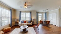 This single-floor residence offers a thoughtfully designed open-concept layout that seamlessly connects the living, dining, and kitchen areas. The spacious living room features rich hardwood-style flooring, crown molding, a ceiling fan, and multiple windows dressed with patterned curtains that fill the space with natural light. Adjacent to the living area, the dining space benefits from a bay window configuration, providing outdoor views and an airy atmosphere.

The kitchen is equipped with rich, dark-stained cabinetry, black appliances including a refrigerator and range, a tile backsplash, and a curved breakfast bar island with a built-in sink — ideal for casual dining or meal prep. A dedicated cabinetry nook with additional counter space and tile backsplash accents the entry hallway.

The primary bedroom is generously sized with plush carpeting, a ceiling fan, and a window overlooking the outdoors. The secondary bedroom also features carpet flooring and a large window with outdoor views. Both bathrooms are finished with dark wood vanities, light stone countertops, tiled tub-and-shower combinations, and hardwood-style flooring. The primary bath includes a dual-sink vanity, offering added convenience. Together, these spaces create a cohesive, comfortable, and well-detailed living environment.