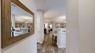 This single-floor, 2-bedroom, 2-bathroom residence offers a cohesive and well-designed layout that maximizes comfort and functionality. Rich wood-look flooring flows throughout the main living areas, complemented by crown molding and neutral gray tones that create a clean, modern aesthetic. The living room features a ceiling fan, large windows with outdoor views, and direct access to a private patio or balcony, filling the space with natural light. Adjacent to the living area, the dining room is defined by wainscoting, pendant lighting, and a decorative wall mirror that enhances the sense of space. The kitchen is equipped with white cabinetry, a tile backsplash, black appliances, and a raised breakfast bar with seating for two, opening conveniently to the dining area. The primary bedroom is generously sized, featuring plush carpet, a window for natural light, and direct access to a dedicated bathroom. The second bedroom also offers carpeted floors, a window, and closet access. Both bathrooms are finished with white vanities, granite-style countertops, and wood-look flooring. One bathroom includes a soaking tub and shower combination. A dedicated in-unit laundry room with shelving completes this thoughtfully planned residence.