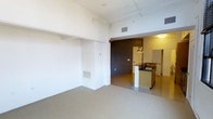 Located at 40 Locke St in Haverhill, Massachusetts, this single-floor space showcases an open-concept layout with a distinctly industrial aesthetic. The generous ceiling height creates an airy, expansive feel throughout, with exposed ductwork and structural elements adding to the raw, urban character of the interior.

The main living area features speckled epoxy flooring that extends seamlessly throughout the space, providing a durable and visually cohesive foundation. Crisp white walls contrast with a bold dark accent wall, creating a striking visual division between the living area and the kitchen zone.

The kitchen is anchored by a peninsula-style island with dark granite-look countertops and white cabinetry, offering both prep space and a casual dining or seating area. Pendant lighting hangs above the island, adding a warm, focused glow to the cooking and gathering space. A doorway beyond the kitchen leads to additional rooms, including what appears to be a bathroom or utility area.

Ventilation is handled through ceiling-mounted HVAC vents, while a wall-mounted unit in the living area provides supplemental climate control. The overall ambiance is clean, minimal, and versatile, making the space well-suited for a variety of uses.