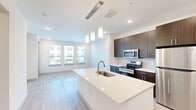 Located in Weatherford, TX, this well-appointed one-bedroom, one-bathroom unit offers a thoughtfully designed open-concept layout across a single floor. The kitchen serves as a centerpiece of the living space, showcasing a large quartz-topped island with an undermount sink and elegant pendant lighting overhead. Dark espresso cabinetry provides ample storage and pairs beautifully with the full suite of stainless steel appliances, including a range, microwave, and refrigerator. Light wood-tone flooring flows throughout the main living areas, enhancing the bright, airy atmosphere created by multiple windows that invite natural light. The living area extends seamlessly from the kitchen, offering a comfortable and functional layout. The bedroom features plush carpeting, a ceiling fan, and a window with natural light, providing a quiet retreat. The bathroom is finished with a wide granite-topped vanity, dark wood cabinetry, brushed nickel hardware, and a large framed mirror illuminated by a modern light bar. A dedicated laundry room includes a full-size washer and dryer, adding everyday convenience. A closet and hallway complete this efficiently organized residence, making it a practical and modern living option.