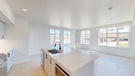 Located in Portland's vibrant NW Savier Street corridor, this modern 2-bedroom, 2-bathroom unit offers a clean, contemporary design throughout. Light wood-tone flooring flows consistently across the entire floor plan, complementing the bright white walls and creating a cohesive, airy aesthetic.

The open-concept kitchen and living area serves as the heart of the unit. The kitchen features a large center island with a white quartz countertop, an undermount sink with a matte black faucet, white cabinetry with black hardware, stainless steel appliances, a gas range, and a decorative tile backsplash. Multiple large windows flood the living area with natural light and offer urban views of the surrounding Portland cityscape.

Both bedrooms are well-proportioned, each featuring oversized windows that invite natural light and provide views of the city. The primary bedroom includes access to a dedicated closet. The primary bathroom is appointed with a dual-sink vanity, quartz countertops, white cabinetry with black hardware, and illuminated LED mirrors. The second bathroom mirrors the modern design with a single vanity and coordinating black fixtures. A hallway with recessed lighting connects the private sleeping quarters to the main living areas, completing this efficiently designed urban residence.