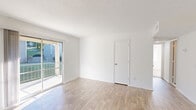 This well-appointed 2-bedroom, 1-bathroom single-floor unit offers a clean, modern aesthetic throughout, characterized by crisp white walls, abundant natural light, and a thoughtful layout. The living room features warm wood-look laminate flooring and a sliding glass door that opens to a private outdoor balcony, allowing natural light to fill the space while providing pleasant outdoor views. Adjacent to the living area, the combined dining and kitchen space is designed for practicality, with white cabinetry, white countertops, and black appliances including a range, refrigerator, and dishwasher, all set over matching wood-look flooring. Both bedrooms are carpeted in neutral tones, offering a comfortable and quiet retreat. The primary bedroom is generously sized, while the secondary bedroom features a window with natural light and a closet with louvered doors. The unit includes four closets in total, providing excellent storage throughout. The full bathroom is finished with white tile surrounding the tub-shower combination, wood-look flooring, and a clean white vanity. A dedicated utility room completes the floor plan. The overall ambiance is light, clean, and move-in ready, with a cohesive neutral palette throughout.