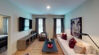 This single-floor residence in Charleston, South Carolina, presents a thoughtfully designed interior with a contemporary aesthetic carried consistently throughout each space. The open-concept layout connects the living area and kitchen, creating a seamless flow ideal for both everyday living and entertaining.

The living room is a standout space, featuring light-toned walls, warm wood-look flooring, and an abundance of natural light admitted through multiple windows dressed with layered blinds and floor-length gray drapes. A large-scale portrait artwork anchors the room, complementing the neutral sofa accented with deep burgundy pillows, a velvet accent chair, and a sleek dark coffee table. A mounted flat-screen television and low-profile media console complete the arrangement.

The kitchen is well-appointed with gray shaker-style cabinetry, granite countertops, stainless steel appliances including a side-by-side refrigerator, range, and built-in microwave, and an island with an undermount sink.

The bedroom features a tall upholstered headboard, ceiling fan, natural light from blinds-fitted windows, and bold abstract wall art. A cozy seating chair adds function to the space.

The bathroom offers a tub-shower combination, granite vanity, wood-look flooring, and clean white tile, maintaining the home's refined, cohesive design.