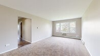Located at 602 Ivarene Ct in Carpentersville, Illinois, this single-floor unit offers a practical and straightforward layout designed for comfortable everyday living. The living area is generously sized, finished with neutral-toned carpet and painted in soft beige tones throughout. A bank of windows along one wall allows ample natural light to filter in while providing views of the surrounding neighborhood. Baseboard heating runs consistently throughout the space, ensuring efficient climate control. A wall-mounted air conditioning unit in the living area adds year-round comfort.

The kitchen features warm oak cabinetry, light countertops, a double stainless steel sink, and a gas range with overhead ventilation. Wood-look flooring grounds the space and transitions seamlessly into adjacent areas. The full bathroom is well-proportioned, offering a single vanity with a large mirror, a tub-shower combination, and wood-look flooring. A second carpeted bedroom provides a window with a green outdoor view and baseboard heating.

Two entry points serve the unit — a wood-toned front door and a secondary exterior door with glazed panels — both bordered by windows that invite additional natural light into the space.