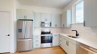 Located at 715 E 36th St in Charlotte's vibrant 28205 corridor, this thoughtfully designed one-bedroom, one-bathroom residence makes efficient use of its single-floor layout. Light wood-tone flooring runs continuously throughout, lending warmth and visual cohesion to every room.

The kitchen is a standout feature, showcasing sage-green flat-front cabinetry with matte black hardware, a subway tile backsplash, white quartz countertops, and a full suite of stainless steel appliances including a French door refrigerator, electric range, over-the-range microwave, and dishwasher. A window above the sink allows natural light to brighten the workspace.

The open-concept layout connects the kitchen seamlessly to the living area, which benefits from large windows that frame views of the surrounding neighborhood and flood the space with daylight. The bedroom continues this bright, airy aesthetic with a generous window and dedicated closet.

The bathroom is appointed with dual undermount sinks set in a long floating vanity matching the kitchen's sage cabinetry, white quartz surfaces, matte black fixtures, framed mirrors, and stylish sconce lighting — creating a clean, modern atmosphere. A dedicated entrance and additional closet storage round out this well-organized residence.