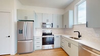 Located at 715 E 36th St in Charlotte's vibrant 28205 corridor, this thoughtfully designed one-bedroom, one-bathroom residence makes efficient use of its single-floor layout. Light wood-tone flooring runs continuously throughout, lending warmth and visual cohesion to every room.

The kitchen is a standout feature, showcasing sage-green flat-front cabinetry with matte black hardware, a subway tile backsplash, white quartz countertops, and a full suite of stainless steel appliances including a French door refrigerator, electric range, over-the-range microwave, and dishwasher. A window above the sink allows natural light to brighten the workspace.

The open-concept layout connects the kitchen seamlessly to the living area, which benefits from large windows that frame views of the surrounding neighborhood and flood the space with daylight. The bedroom continues this bright, airy aesthetic with a generous window and dedicated closet.

The bathroom is appointed with dual undermount sinks set in a long floating vanity matching the kitchen's sage cabinetry, white quartz surfaces, matte black fixtures, framed mirrors, and stylish sconce lighting — creating a clean, modern atmosphere. A dedicated entrance and additional closet storage round out this well-organized residence.