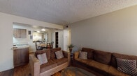 This single-story residence offers a well-organized layout that balances comfort and functionality throughout its key living areas. The living room is a welcoming, open space finished with hardwood-style flooring, a textured ceiling, and a large sliding glass door fitted with vertical blinds that allows natural light to fill the room while providing access to the exterior. The adjoining dining area features a ceiling fan, a built-in shelving unit, and a large wall mirror that enhances the sense of space and reflects the natural light from nearby windows. The kitchen is equipped with warm oak-toned cabinetry, a double-basin stainless steel sink, laminate countertops, and a full-size refrigerator, all set atop matching hardwood-style flooring. The two bedrooms are carpeted for comfort and each feature windows with horizontal blinds that let in soft, natural light. Both bathrooms share a consistent design with wood-tone vanity cabinetry, single-basin sinks with laminate countertops, large mirrors, and shower/tub combinations. The space maintains a cohesive neutral color palette throughout, with textured ceilings and warm-toned walls creating a practical and comfortable living environment.