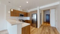 This contemporary single-floor residence showcases a thoughtfully designed open-concept layout with high-quality finishes throughout. The kitchen is a standout feature, equipped with warm wood-tone flat-panel cabinetry extending to the ceiling, stainless steel appliances including a refrigerator, range, and microwave, a crisp white tile backsplash, and a white quartz peninsula that seamlessly connects to the living area. Light wood-look flooring flows throughout the main living spaces, lending warmth and continuity to the design.

The living area is bright and airy, benefiting from large sliding glass doors that open to a private balcony offering open city views. The bedroom includes plush carpeting and a generous sliding-door closet with double hanging rods, providing ample storage. The bathrooms are elegantly finished with large-format tile flooring, wood-tone vanities topped with white countertops, and oversized mirrors. The full bathroom features a soaking tub with floor-to-ceiling marble-style tile surround, while a second bathroom offers a clean, minimalist vanity design. Recessed lighting throughout ensures a bright, welcoming ambiance in every room.