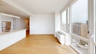 Located at 1 Ocean Dr in Brooklyn's Coney Island neighborhood, this well-appointed 2-bedroom, 2-bathroom residence offers a clean, modern aesthetic throughout. Light-toned hardwood flooring flows seamlessly across the entire living space, complementing the bright white walls and creating a warm, airy atmosphere.

The open-plan kitchen and living area serves as the heart of the home. The kitchen features sleek white cabinetry, a large central island with a stone countertop and undermount sink, stainless steel appliances, and a subway tile backsplash. The living area is bathed in natural light through expansive floor-to-ceiling windows that frame sweeping panoramic views of the ocean and Brooklyn skyline, with direct access to a private balcony.

Both bedrooms are generously sized, with large windows offering beautiful water and city views, and ample closet space — four closets are distributed throughout the residence. The primary bedroom benefits from its own dedicated access to the hallway and closets.

The two full bathrooms are finished with striking marble-style wall tiles, warm beige stone-tile flooring, wood-toned vanities, and tub-shower combinations. Additional conveniences include an in-unit laundry area and a well-lit hallway with recessed lighting connecting all areas of the home.