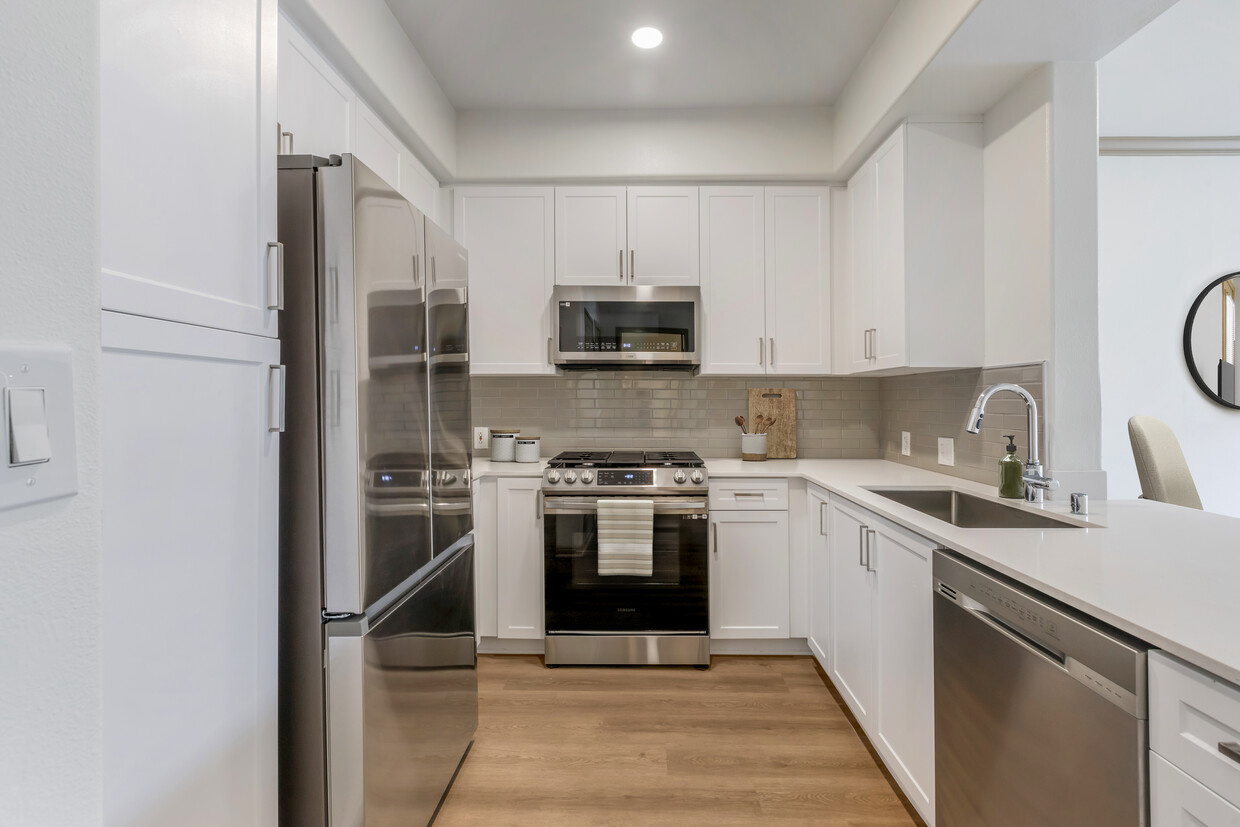 Renovated Package I kitchen with stainless steel appliances, white speckled quartz countertop, white cabinetry, grey tile backsplash, and hard surface flooring - Avalon Thousand Oaks Plaza