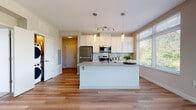 Located at 2809 Clinton Ave in Cleveland's vibrant Ohio City neighborhood, this single-floor residence offers a thoughtfully designed open-concept layout with clean, contemporary finishes throughout. The kitchen serves as the heart of the home, showcasing white shaker cabinetry, stainless steel appliances including a refrigerator, microwave, and range, a subway tile backsplash, and a generous central island with pendant lighting overhead. Large windows flood both the kitchen and adjacent living area with abundant natural light and provide pleasant views of the surrounding greenery. The living space features warm hardwood-style flooring that extends seamlessly through the main living areas, creating a cohesive and inviting atmosphere. The bedrooms are carpeted for comfort and each benefit from multiple windows that bring in natural light. The bathroom is finished with a walk-in glass-enclosed shower accented by white tile, complemented by hardwood-style flooring for a sleek, modern look. A dedicated in-unit laundry closet with a stacked washer and dryer adds everyday convenience. The overall design emphasizes brightness, clean lines, and functional living in a well-appointed modern space.