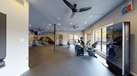 Located at 3475 Pleasant Hill Rd in Duluth, GA, this fitness center offers a comprehensive and thoughtfully designed exercise space across a single open floor. The room is finished with durable dark rubber flooring throughout, providing a safe and functional surface for a wide variety of workouts. Recessed lighting paired with multiple ceiling fans ensures the space remains well-lit and comfortably ventilated during any activity.

The cardio section is well-appointed with equipment including elliptical trainers, stationary bikes, a rowing machine, a Peloton bike, a treadmill, and a Jacobs Ladder climber. A dedicated strength training area features a multi-function cable machine, offering users a full-body workout experience. Wall-mounted flat-screen televisions are positioned throughout, providing entertainment during workouts.

Large windows along multiple walls flood the space with natural light and offer views of the surrounding greenery, creating an inviting and energizing atmosphere. A full-length mirror along one wall visually expands the room and supports form-checking during exercise. The fitness center is accessed through a glass-panel door and is clearly marked with posted cardio center rules. The overall design is clean, modern, and practical, making it a well-rounded facility suited for a broad range of fitness needs.