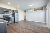 Located at 1055 Simon Crestway in Waunakee, WI, this efficiently designed one-bedroom, one-bathroom residence offers a thoughtful layout with modern finishes throughout. Light wood-tone luxury vinyl plank flooring flows through the main living areas, lending a clean and contemporary feel.

The open-concept kitchen and living room serve as the heart of the space. The kitchen is equipped with rich, dark-stained cabinetry, granite-style countertops, a stainless steel sink, and a full suite of stainless steel appliances including a range, microwave, and refrigerator. Recessed lighting illuminates the kitchen, while the adjoining living area benefits from a wall-mounted mini-split HVAC unit for year-round climate control.

The living room is bright and welcoming, featuring a sliding glass door that opens to a private balcony with a railed exterior, as well as an additional window that floods the room with natural light. The bedroom is carpeted for comfort and includes built-in wire shelving for storage, with a high horizontal window that brings in additional natural light. The full bathroom features wood-look flooring, a tub-shower combination with a curtain rod, and clean white finishes throughout.