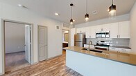 This single-floor, one-bedroom, one-bathroom unit in Colorado Springs, CO offers a well-designed layout that maximizes its compact footprint. The open-concept kitchen and living area serves as the heart of the space, featuring light wood-style flooring that flows throughout. The kitchen is equipped with stainless steel appliances, including a refrigerator, electric range, and microwave, complemented by crisp white cabinetry with black hardware and a tile backsplash. A central island with a warm-toned countertop and an undermount sink doubles as a breakfast bar, illuminated overhead by a trio of stylish pendant lights. The living area receives natural light through windows that overlook the surrounding neighborhood. The bedroom features soft carpeting, a window with a blind, and access to a dedicated closet. The bathroom is finished with wood-style flooring, a dark-toned vanity with a white countertop, and a tiled tub-shower combination. An in-unit laundry area adds everyday convenience. Neutral tones and modern finishes give the entire space a clean, contemporary character.