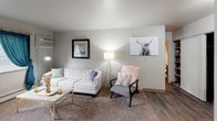 Located at 1422 Preston Ridge NW in Walker, Michigan, this single-floor unit offers a thoughtfully laid-out living space with a warm and welcoming ambiance. The open living area is finished with a mix of plush carpet and wood-look hard flooring, creating a comfortable yet stylish foundation throughout. Large windows fitted with blinds allow natural light to fill each room, enhancing the bright, airy atmosphere. The living room provides generous space for seating and relaxation, with neutral-toned walls that complement a variety of décor styles. Adjacent to the living area, the kitchen is outfitted with rich, dark cabinetry featuring modern hardware, light-toned countertops, a double-basin stainless steel sink, and white appliances including a dishwasher and refrigerator — offering both function and a clean aesthetic. The bedroom is a cozy retreat, featuring soft carpeting, a well-sized window dressed with sheer curtains, and ample room for a full furniture arrangement. Closet storage is also visible within the unit's layout. Overall, the space presents a practical and comfortable single-floor layout well-suited for everyday living in the Walker, MI community.