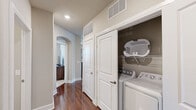 Located at 1501 Meridian Dr in Irving, TX, this well-appointed 2-bedroom, 2-bathroom residence offers a thoughtfully designed single-level layout. The open-concept living, dining, and kitchen area serves as the heart of the home, anchored by rich hardwood-style flooring that flows throughout the main spaces. The kitchen is outfitted with dark espresso cabinetry, stainless steel appliances including a refrigerator, range, microwave, and dishwasher, and a white quartz-topped island with bar seating — ideal for casual dining or entertaining. The living room is bright and welcoming, featuring multiple windows with horizontal blinds that invite natural light, a ceiling fan, and access to a private balcony overlooking a scenic outdoor view. Each bedroom is carpeted for comfort and equipped with a ceiling fan and dedicated closet space. The spacious primary bedroom includes direct access to its own bathroom, which features dark wood vanity cabinetry, white countertops, and a walk-in closet with built-in shelving. A second full bathroom serves the additional bedroom and guests. A hallway laundry area with a full-size washer and dryer adds everyday convenience. The neutral color palette and clean architectural lines throughout lend the space a modern, cohesive feel.