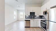 This efficiently designed single-floor unit combines contemporary finishes with a clean, modern aesthetic. The open-concept kitchen and living area forms the heart of the space, featuring light hardwood-style flooring that extends throughout the unit, creating a seamless and cohesive feel. The kitchen is well-appointed with white shaker-style cabinetry reaching toward the ceiling, a bold dark subway tile backsplash, white quartz countertops, and a full suite of stainless steel appliances including a range, microwave, dishwasher, and refrigerator. Multiple windows in the living area allow natural light to fill the space, contributing to an open and airy atmosphere.

The bedroom offers multiple windows with views of the surrounding area, fitted with blinds for privacy and light control. Crisp white walls and light flooring maintain the unit's bright, neutral palette. A dedicated closet provides practical storage.

The bathroom is finished with a white vanity topped with granite countertops, brushed nickel hardware, wood-look flooring, and a glass-enclosed shower, reflecting the same modern sensibility found throughout the unit. Overall, the space presents a clean, contemporary design well-suited for efficient single-occupant living.