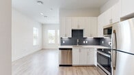 This efficiently designed single-floor unit combines contemporary finishes with a clean, modern aesthetic. The open-concept kitchen and living area forms the heart of the space, featuring light hardwood-style flooring that extends throughout the unit, creating a seamless and cohesive feel. The kitchen is well-appointed with white shaker-style cabinetry reaching toward the ceiling, a bold dark subway tile backsplash, white quartz countertops, and a full suite of stainless steel appliances including a range, microwave, dishwasher, and refrigerator. Multiple windows in the living area allow natural light to fill the space, contributing to an open and airy atmosphere.

The bedroom offers multiple windows with views of the surrounding area, fitted with blinds for privacy and light control. Crisp white walls and light flooring maintain the unit's bright, neutral palette. A dedicated closet provides practical storage.

The bathroom is finished with a white vanity topped with granite countertops, brushed nickel hardware, wood-look flooring, and a glass-enclosed shower, reflecting the same modern sensibility found throughout the unit. Overall, the space presents a clean, contemporary design well-suited for efficient single-occupant living.