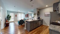 Located at 555 5th Ave. in Columbus, Ohio, this single-floor residence offers a well-designed open-concept layout that seamlessly connects the kitchen, dining, and living areas. The kitchen is a functional centerpiece, featuring gray shaker-style cabinetry, granite countertops, a large island with an undermount sink and pendant lighting, and a full suite of stainless steel appliances. Warm hardwood-style flooring runs throughout the main living areas, adding continuity and a welcoming feel. The living room is bright and airy, benefiting from large windows dressed with sheer curtains that allow generous natural light to filter in. A glass door provides direct access to an outdoor area. The space includes two bedrooms, each carpeted and outfitted with windows that bring in natural light and views of the surrounding greenery. Both bathrooms are finished with large-format tile flooring, dark wood vanities with granite countertops, and glass-enclosed shower/tub combinations. The overall aesthetic throughout the residence is modern and cohesive, with soft gray walls, recessed lighting, and thoughtful design details that create a comfortable, contemporary living environment.