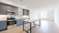 Located at 225 N Sycamore St in Wichita, Kansas, this thoughtfully designed one-bedroom, one-bathroom unit offers a contemporary living experience with a clean, modern aesthetic throughout. The open-concept kitchen and living area serves as the heart of the space, featuring sleek slate-blue cabinetry, white subway tile backsplash, stainless steel appliances including a range, microwave, and refrigerator, and a central island with a light countertop that doubles as a dining or workspace. Light wood-tone flooring flows throughout the main living areas, complementing the bright white walls and recessed lighting. Large windows invite generous natural light into the living room, which also provides direct access to a private balcony with outdoor views. The bedroom is a comfortable retreat finished with plush carpet, a ceiling fan, and a sizable window framing exterior views. The full bathroom is clean and modern, outfitted with large-format floor tiles, a soaking tub with shower, and a floating vanity with a white countertop. A dedicated laundry area houses a full-size top-loading washer and dryer, adding everyday convenience. The overall ambiance is fresh, bright, and move-in ready.