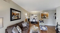 This renovated two-bedroom, two-bathroom South Hampton residence is thoughtfully designed across a single floor, offering an open and connected layout that maximizes both function and comfort. The living area serves as the heart of the home, featuring warm hardwood flooring, neutral-toned walls, and ample space for comfortable furnishings. A large decorative mirror adds depth to the living room, enhancing the sense of openness throughout the space. The living area flows seamlessly into the dining space, which is highlighted by a pendant light fixture that anchors the dining area with a stylish focal point. Beyond the dining space, the kitchen is equipped with wood cabinetry, modern appliances including a range with overhead microwave, and a breakfast bar that provides additional seating and prep space. The open sightlines between the kitchen, dining, and living areas create a cohesive and airy feel throughout the main living space. The renovation brings updated finishes and a clean, contemporary aesthetic to the entire residence, making it a well-appointed and move-in-ready home with a welcoming ambiance.