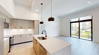 Located in Miami, FL, this well-appointed 3-bedroom, 2-bathroom unit offers a thoughtfully designed single-floor layout with modern finishes throughout. Light wood-tone flooring flows seamlessly across the living areas and bedrooms, creating a bright and cohesive aesthetic complemented by crisp white walls.

The open-concept kitchen and living room serve as the heart of the home. The kitchen is outfitted with light wood cabinetry featuring matte black hardware, white quartz countertops, stainless steel appliances including a refrigerator, range, and over-the-range microwave, and a central island with an integrated sink — all beneath soaring ceilings with a statement pendant light.

The primary bedroom offers comfortable proportions and connects to a walk-in closet finished with marble-look tile flooring and wire shelving. Bedrooms feature large floor-to-ceiling windows and sliding glass doors opening to a private balcony with views of palm trees and lush greenery. The bathrooms are finished with elegant marble-patterned tile surrounding a soaking tub and shower combination.

Additional highlights include a dedicated laundry room with a stacked washer and dryer, two closets, and a connecting hallway. The overall ambiance is clean, contemporary, and move-in ready.