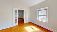 Located at 6300 N Rosebury Ave in Clayton, MO, this one-bedroom, one-bathroom residence offers a well-organized, single-floor layout that makes efficient use of its cozy footprint. Warm hardwood floors run throughout the living areas and bedroom, lending a timeless character to the space. The living room is highlighted by elegant French doors with glass pane detailing, which allow natural light to flow between rooms while creating a refined visual connection. Multiple windows throughout the unit frame views of lush green surroundings, further brightening the neutral, cream-toned walls. The bedroom is a comfortable, well-proportioned room with its own window overlooking the outdoors and includes a closet for ample storage. The kitchen is outfitted with white shaker-style cabinetry, dark countertops, a gas range, and stainless appliances, all set atop marble-look tile flooring that contrasts cleanly with the subway tile backsplash. A dedicated entrance and two hallways provide a functional flow through the unit. The bathroom features a classic tub-shower combination with full white subway tile surround, maintaining a clean, bright aesthetic. Overall, the space presents a classic yet updated feel, ideal for comfortable single-occupancy living in the heart of Clayton.