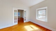 Located at 6300 N Rosebury Ave in Clayton, MO, this one-bedroom, one-bathroom residence offers a well-organized, single-floor layout that makes efficient use of its cozy footprint. Warm hardwood floors run throughout the living areas and bedroom, lending a timeless character to the space. The living room is highlighted by elegant French doors with glass pane detailing, which allow natural light to flow between rooms while creating a refined visual connection. Multiple windows throughout the unit frame views of lush green surroundings, further brightening the neutral, cream-toned walls. The bedroom is a comfortable, well-proportioned room with its own window overlooking the outdoors and includes a closet for ample storage. The kitchen is outfitted with white shaker-style cabinetry, dark countertops, a gas range, and stainless appliances, all set atop marble-look tile flooring that contrasts cleanly with the subway tile backsplash. A dedicated entrance and two hallways provide a functional flow through the unit. The bathroom features a classic tub-shower combination with full white subway tile surround, maintaining a clean, bright aesthetic. Overall, the space presents a classic yet updated feel, ideal for comfortable single-occupancy living in the heart of Clayton.