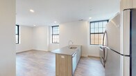 Located at 1 Atlantic St in the heart of downtown Stamford, CT, this thoughtfully designed single-floor unit showcases a clean, contemporary aesthetic throughout. Light wood plank flooring flows seamlessly across the open living and kitchen areas, creating a warm and cohesive atmosphere. Large black-framed windows invite abundant natural light into every room while offering views of the surrounding urban streetscape.

The kitchen is a standout feature, centered around a generously sized island with a quartz countertop and integrated sink with a modern arc faucet. Light wood cabinetry lines the walls alongside stainless steel appliances, including a range, refrigerator, and dishwasher, all complemented by a subway tile backsplash and under-cabinet range hood.

The living and bedroom areas are bright and open, with crisp white walls, recessed lighting, and ample room for flexible arrangements. Each space benefits from the natural light provided by the prominent black-framed windows.

The bathroom is finished with large-format gray tile flooring, a vanity with wood-toned cabinetry, and a walk-in shower equipped with both a fixed showerhead and handheld fixture, along with grab bars. White shaker-style interior doors with matte black hardware add a refined, modern touch throughout the unit.