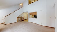 This two-story residence offers a thoughtfully designed layout that maximizes space and functionality across both levels. The main floor centers around a generous living area distinguished by dramatic vaulted ceilings and a striking open staircase with warm wood railings. A sliding glass door floods the room with natural light and provides direct access to an outdoor balcony with views of surrounding trees. Ceiling fans are present throughout, contributing to year-round comfort.

The kitchen features abundant oak cabinetry, white countertops, and a full suite of black appliances including a refrigerator, range, and dishwasher. A pass-through counter connects the kitchen to the living area, enhancing the open feel of the main floor. Tile flooring provides a practical surface in both the kitchen and bathrooms, while plush carpeting runs throughout the living spaces and bedrooms.

Upstairs, multiple bedrooms offer comfortable retreats, including one with vaulted ceilings and a ceiling fan, and another with a closet and a window overlooking the exterior. Two full bathrooms serve the home — one featuring a walk-in shower and tile flooring, the other with a full tub/shower combo, a wide vanity with oak cabinetry, and a large mirror. Baseboard heating is present throughout, ensuring consistent warmth across all rooms.