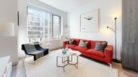 Located at 1177 Market St in the heart of San Francisco, this contemporary single-floor residence offers a well-designed layout with a clean, modern aesthetic throughout. The kitchen is outfitted with high-gloss cabinetry in deep slate blue and weathered wood tones, stainless steel appliances including a full-size refrigerator, built-in microwave, and range, complemented by light wood-style flooring and under-cabinet lighting. A stainless steel prep island with a lower storage rack adds functional versatility to the space. The open living area is bathed in natural light from large city-facing windows that frame views of the surrounding San Francisco skyline. Crisp white walls serve as a neutral backdrop, allowing bold accent pieces to stand out. The primary bedroom continues the bright, airy aesthetic with large windows offering urban views and vibrant wall art. A secondary room features a convertible wall-desk unit, making it ideal for use as a home office or guest space. The bathroom is a standout feature, finished in floor-to-ceiling marble-look tile with a glass-enclosed walk-in shower and polished chrome fixtures. Throughout, the residence balances contemporary design with practical living in one of San Francisco's most central neighborhoods.