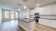 This well-designed single-story home offers two bedrooms and two bathrooms within a thoughtfully laid-out floor plan. The open-concept kitchen and living area serves as the heart of the home, anchored by a large center island with a striking dark granite countertop, an integrated sink, and globe pendant lighting overhead. White shaker cabinetry, a classic subway tile backsplash, and stainless steel appliances — including a gas range and French door refrigerator — complete the kitchen's clean, contemporary aesthetic. Light wood-tone hardwood flooring flows throughout the entire home, enhancing the bright and airy atmosphere. The living area features a ceiling fan and access to the outdoors through a glass door flanked by windows, filling the space with natural light. The primary bedroom is generously sized, accompanied by a private en-suite bathroom with white cabinetry, dark granite countertops, a glass-enclosed shower with marble tile surround, and direct access to a spacious walk-in closet with dual hanging rods and built-in shelving. The second bedroom also benefits from natural light through a large window and includes its own ceiling fan. A second full bathroom serves the additional bedroom. Two closets provide ample storage throughout the home.