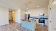 Located at 1532 Hammond Rd W in Traverse City, Michigan, this well-appointed 2-bedroom, 2-bathroom residence offers a clean, modern aesthetic throughout its single-level layout. Light-toned luxury vinyl plank flooring runs continuously through the space, creating a cohesive and easy-to-maintain foundation in every room.

The open-concept kitchen and living area serves as the heart of the home. The kitchen is outfitted with stainless steel appliances, crisp white cabinetry extending to the ceiling, dark countertops, and a central island with a built-in sink — illuminated by three stylish pendant lights with brass accents. A tall pantry cabinet provides additional storage near the kitchen's edge.

The living area features a sliding glass door that opens to a private outdoor deck, filling the space with natural light and offering pleasant views of the surrounding landscape. The primary bedroom is a comfortable size and includes a ceiling fan, while the second bedroom also benefits from natural light through a window with outdoor views.

Both bathrooms are finished in a clean, neutral palette. The primary bath features an elongated vanity with white cabinetry and grab bar-equipped walls, while the second bath includes a tub/shower combo and a white vanity with a large mirror. A dedicated laundry room houses a full-size washer and dryer with overhead wire shelving for added convenience.