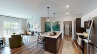 This single-floor residence showcases a thoughtfully designed open-concept layout with contemporary finishes throughout. Wood-look flooring flows seamlessly across the main living areas, anchoring the space with warmth and cohesion.

The kitchen serves as a central hub, featuring dark espresso cabinetry paired with crisp white upper cabinets and a light subway tile backsplash. A large island with seating for multiple provides both additional workspace and a casual dining option, illuminated overhead by stylish Edison-bulb pendant lights. Stainless steel appliances, including a refrigerator, range, and microwave, complete the setup. A dedicated in-unit laundry area with a stacked washer and dryer is conveniently accessible nearby.

The living area offers generous proportions, with a sliding glass door that opens onto a private balcony, inviting natural light and outdoor views of surrounding greenery. The two bedrooms are well-sized, each featuring large windows that further enhance the bright, airy atmosphere.

Two full bathrooms serve the residence. One includes a soaking tub and shower combination with dark wood vanity cabinetry and a wide mirror, while the second features a streamlined vanity with ample counter space. Together, the interiors present a clean, modern aesthetic suited for comfortable everyday living.